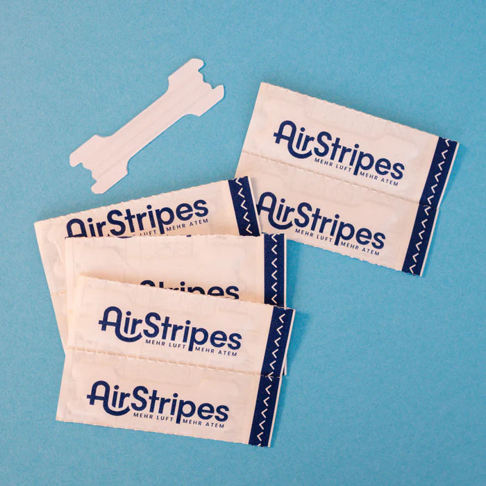 Mehrere verpackte Airstripes Nasenpflaster auf blauem Hintergrund – Produktfoto der transparenten Nasenpflaster mit Markenaufdruck.