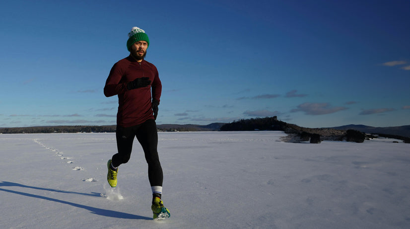 Ein Jogger mit Mütze, Sportkleidung und Nasenpflaster läuft bei Sonnenschein über eine schneebedeckte Fläche